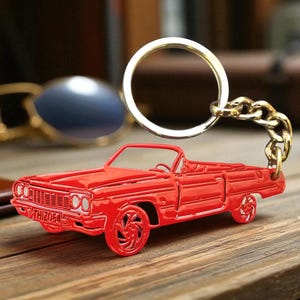 May include: A bright red metal keyring shaped like a classic convertible car. The car features detailed wheels, a front grille, and a number plate with the text THIZ054. A silver-toned metal split ring is attached to the car by a short chain.
