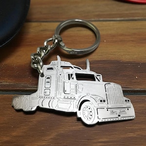 May include: A silver-toned metal keychain featuring a detailed cutout silhouette of a semi-truck. The truck design includes a prominent front grille, exhaust stacks, and wheels. The text "Big Jim" is engraved on the front bumper area.