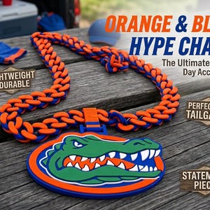 May include: A thick, chunky chain necklace featuring alternating orange and blue links. A large, circular pendant hangs from the center, displaying a green alligator head graphic with white teeth on an orange and blue background. Text reads ORANGE & BLUE HYPE CHAIN.