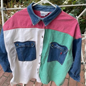 May include: A long-sleeve button-down shirt featuring a colour-blocked design with a blue denim collar, pink upper panels, a white left panel, a green right panel, and dark blue denim sleeves and chest pockets with metal buttons and a red tab.