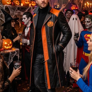Könnte beinhalten: Ein langer schwarzer Ledermantel mit leuchtend orangefarbenen Revers und Besätzen sowie einer kleinen orangefarbenen Kürbisgrafik auf der linken Brust. Der Mantel wird über einem schwarzen Rollkragenpullover und einer dunkelgrauen Jeans getragen.