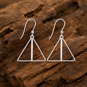 May include: A pair of silver-toned earrings featuring a geometric triangle design. Each earring consists of a thin triangular wire frame with a vertical bar running through the centre, suspended from a curved hook for pierced ears.