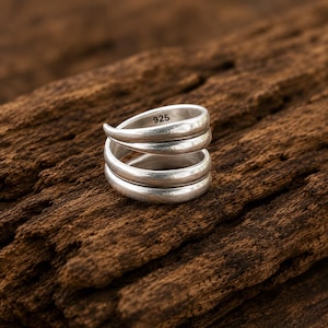 May include: A silver ring with a bypass wrap design featuring two smooth, rounded bands that overlap. The interior of the band is clearly stamped with the hallmark 925, indicating sterling silver composition. The metal has a matte finish.