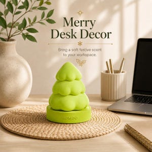 May include: A lime green, three-tiered, tree-shaped object with a rounded base featuring the embossed text "HOMOO". The text "Merry Desk Decor" and "Bring a soft festive scent to your workspace" is printed above the object in dark green lettering.