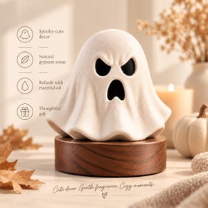 May include: A white ghost-shaped gypsum stone diffuser with black eye and mouth cutouts, resting on a circular dark wood base. Text on the left lists features: Spooky-cute decor, Natural gypsum stone, Refresh with essential oil, Thoughtful gift.