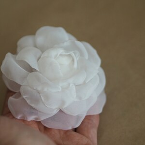 May include: A white fabric flower with a delicate, layered design. The flower is made of soft, sheer fabric and has a slightly ruffled appearance.