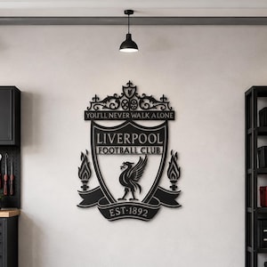 Può includere: Un'opera d'arte da parete in metallo nero raffigurante lo stemma del Liverpool Football Club, con l'emblema del Liver bird, il testo "YOU'LL NEVER WALK ALONE", "LIVERPOOL FOOTBALL CLUB" e "EST 1892", montata al centro di una parete chiara.