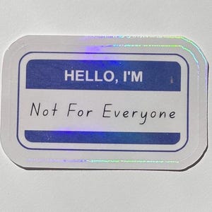 May include: A rectangular holographic sticker featuring a blue and white name tag design. The text HELLO, I'M is printed in white capital letters on a blue background, followed by the phrase Not For Everyone in black cursive script below.