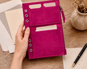 May include: A vibrant magenta suede planner cover featuring a vertical zipper closure, three silver-toned metal eyelets along the left edge, and multiple interior pockets designed to hold cards and documents in a structured, organized layout.