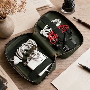 May include: An open olive green leather zipped organiser case featuring internal elastic straps and pockets. The case contains various white, red, and black charging cables, a white power adapter, and a black wall plug, all neatly secured inside.