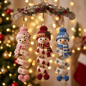 Puede incluir: Tres adornos de muñecos de nieve tejidos a ganchillo que cuelgan de un arco de madera decorativo. Cada muñeco lleva un gorro y una bufanda de punto, con un cuerpo en espiral que presenta cuentas y dijes. Rosa, rojo y azul respectivamente.