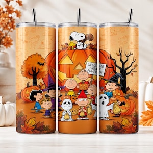 May include: A cylindrical stainless steel tumbler with a straw, featuring a Peanuts Halloween graphic with Snoopy, Charlie Brown, and friends around a large jack-o'-lantern. The design includes a sign that reads WELCOME GREAT PUMPKIN on an orange background.