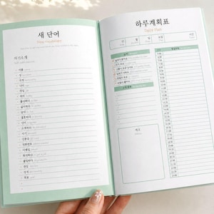 Peut inclure: Un agenda ouvert aux pages vert clair présentant une section Nouveau vocabulaire avec des termes coréens et anglais pour se présenter à gauche, et un planning quotidien avec des icônes météo et des horaires à droite.