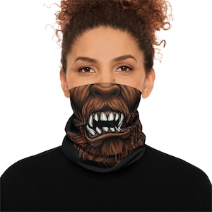 May include: A black neck gaiter featuring a graphic print of a brown, furry creature with a prominent nose and sharp, white bared teeth. The design covers the front of the fabric, displaying detailed fur textures and a snarling expression.