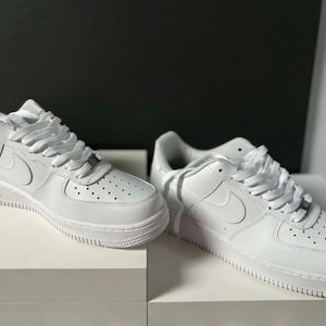 Può includere: Un paio di sneakers basse bianche con tomaia in pelle liscia, punta traforata per la ventilazione, lacci bianchi abbinati e logo swoosh tonale sul lato. Le scarpe presentano una spessa suola in gomma e un dubrae metallico alla base dei lacci.