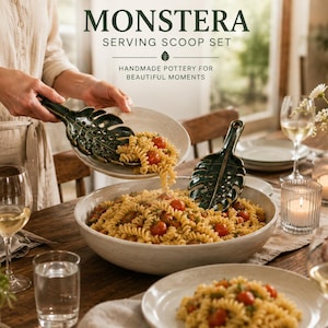 May include: A set of two dark green ceramic serving scoops shaped like monstera leaves, used to serve pasta with cherry tomatoes from a large, shallow, light-colored ceramic bowl. The text MONSTERA SERVING SCOOP SET is visible above.