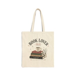 May include: A cream-colored canvas tote bag featuring a graphic of a stack of books topped with a coffee mug. The text reads BOOK LOVER, JUST ONE MORE CHAPTER, BOOKS COFFEE PEACE, and SO MANY BOOKS, SO LITTLE TIME, with small heart and floral accents.