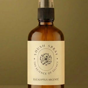 Può includere: Un flacone spray in vetro ambrato con erogatore nero e un'etichetta color crema. L'etichetta presenta un'illustrazione di un dente di leone, il testo SHUSH SPRAY, THE SCIENCE OF SILENCE e EUCALYPTUS ARGENTÉ in caratteri neri senza grazie.