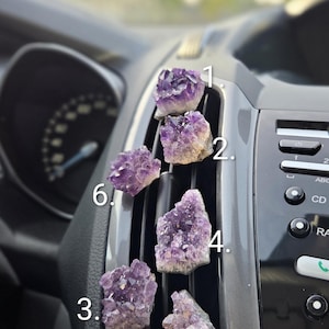 Könnte beinhalten: Sechs kleine, rohe Amethyst-Kristallcluster mit tiefvioletten, gezackten Spitzen und gräulich-weißen felsigen Basen. Jedes Cluster ist von eins bis sechs nummeriert und vertikal entlang der dunkelgrauen Kunststofflamellen einer Autolüftung angeordnet.