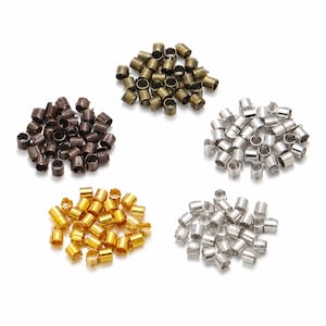 Puede incluir: Una colección de pequeñas cuentas de metal cilíndricas dispuestas en cinco montones distintos. Los colores incluyen bronce antiguo, marrón oscuro, oro brillante, plata pulida y un acabado en plata mate, cada una con un centro hueco.