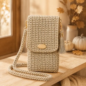 May include: A beige crochet crossbody bag featuring a rectangular body with a flap closure, a matching long strap, and a gold-toned oval accent on the front. A decorative matching tassel hangs from a gold-toned metal clip on the side of the bag.