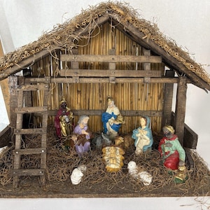May include: A wooden nativity scene set featuring a stable with a thatched roof, a ladder, and straw flooring. The set includes hand-painted figurines of the Holy Family, three wise men, and animals. A wooden ruler is visible on the left side.