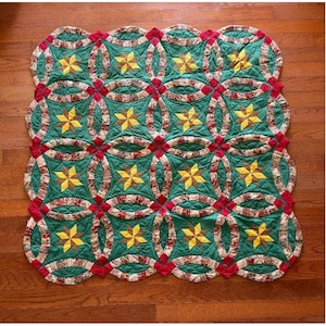 May include: A square quilt featuring a repeating pattern of green fabric squares, each centered with a yellow six-pointed star. The design is framed by interlocking oval shapes in a multi-colored floral print with red accents.