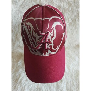 May include: A maroon baseball cap featuring a large, cream-colored graphic of an elephant head on the front panels. A prominent, embroidered maroon letter A is centered over the elephant design. The cap has a solid maroon brim and a button top.