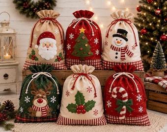 May include: Six fabric drawstring gift bags featuring Christmas designs including Santa Claus, a decorated pine tree, a snowman, a reindeer, holly leaves with berries, and a candy cane, all accented with white snowflakes and plaid trim.