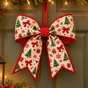 May include: A large decorative bow made of off-white fabric featuring a repeating pattern of green Christmas trees, red gift boxes, red bows, and red snowflakes. The bow has a red piped edge and a central knot with a white polka dot pattern.