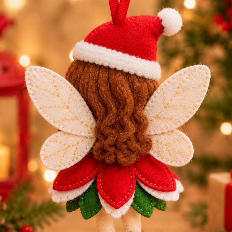 K&ouml;nnte beinhalten: Ein Feen-Anh&auml;nger aus Filz mit braunem Garnhaar, einer roten Weihnachtsm&uuml;tze mit wei&szlig;em Bommel und cremefarbenen Fl&uuml;geln mit gestickten Aderdetails. Die Fee tr&auml;gt einen Lagenrock aus roten und gr&uuml;nen Filzbl&uuml;ten und hat eine Aufh&auml;ngeschlaufe.
