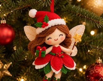 May include: A felt Christmas ornament shaped like a fairy with brown hair, wearing a red Santa hat with holly, a red dress with green leaves, and white wings. The fairy holds a small green gift box and a yellow star wand, hanging by a red ribbon.