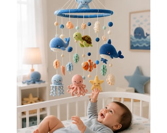 May include: A hanging nursery mobile featuring crocheted sea creatures including a blue whale, a green turtle, an orange clownfish, a pink octopus, and a yellow starfish suspended from a blue ring with a light blue star at the top center.