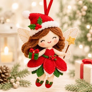 K&ouml;nnte beinhalten: Ein Filz-Feen-Anh&auml;nger mit braunem Haar, einer roten Weihnachtsmannm&uuml;tze mit Stechpalme und einem rot-gr&uuml;nen Bl&uuml;tenblattkleid. Die Fee h&auml;lt ein kleines gr&uuml;nes Geschenk mit roter Schleife und einen gelben Sternenstab, erg&auml;nzt durch wei&szlig;e Fl&uuml;gel.