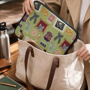Puede incluir: Una funda rectangular para portátil con fondo verde claro que presenta un collage de diversas ilustraciones que incluyen gatos, pretzels, lazos, cámaras, mapas, un teléfono y un tranvía, todo ello encerrado en un borde con cremallera negra.