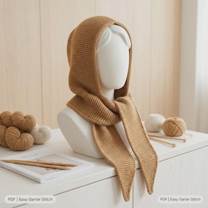 May include: A tan knitted hood with long scarf ends, crafted in a garter stitch pattern. The hood is displayed on a white mannequin head. The text "PDF | Easy Garter Stitch" is visible at the bottom corners of the image.