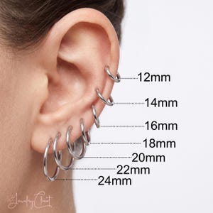 May include: A series of seven silver-toned hoop earrings arranged in a vertical line along the earlobe and cartilage. Each hoop is labelled with its corresponding diameter, ranging from 12mm at the top to 24mm at the bottom, in 2mm increments.