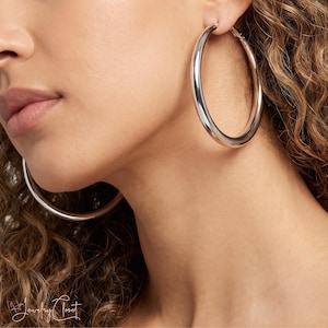 May include: A pair of large, polished silver-tone hoop earrings with a smooth, rounded tubular design. The earrings feature a classic circular shape with a reflective metallic finish, showcasing a simple and clean aesthetic for everyday wear.