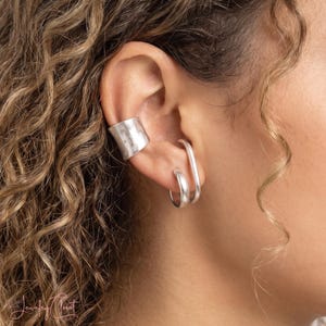 Puede incluir: Un pendiente tipo ear cuff plateado con textura martillada ancha se sit&uacute;a en el cart&iacute;lago superior, mientras que un aro plateado alargado y liso y otro aro plateado m&aacute;s peque&ntilde;o y sencillo se colocan en el l&oacute;bulo inferior de la oreja.