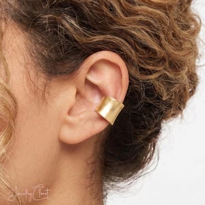 Puede incluir: Un ear cuff ancho de metal dorado con acabado liso y pulido. Esta pieza de joyer&iacute;a se coloca en el cart&iacute;lago de la oreja, envolviendo la concha para crear una apariencia de banda s&oacute;lida sin necesidad de tener perforaciones en la oreja.