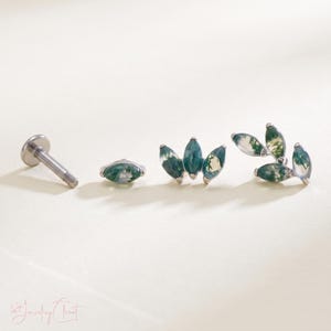 May include: A set of body jewelry components featuring moss agate stones in marquise cuts. The set includes a threaded metal post, a single marquise stone stud, a three-stone cluster piece, and a four-stone branch-like cluster piece in silver.