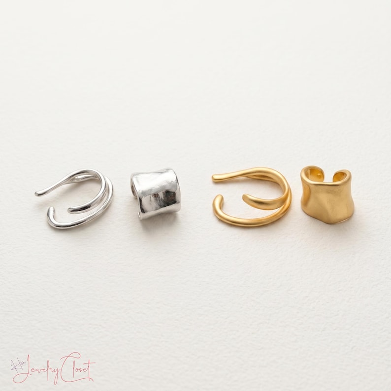 Puede incluir: Cuatro pendientes tipo ear cuff dispuestos en fila. Dos son de tono plateado, uno con dise&ntilde;o de doble banda y otro con una superficie lisa, ancha y curva. Dos son de tono dorado, uno con dise&ntilde;o de doble banda y otro con una superficie lisa.