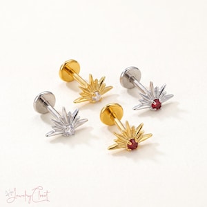 May include: Four flat-back stud earrings featuring a sunburst design. Two earrings are gold-toned with a red center stone, and two are silver-toned with a clear center stone. Each stud has a circular base and a radiating starburst metal frame.