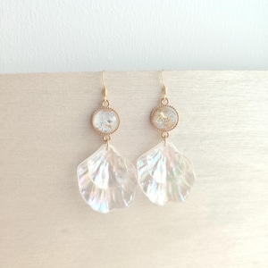 May include: A pair of gold-toned drop earrings featuring a circular stud with embedded metallic flakes, connected to a translucent, iridescent, shell-shaped pendant. The earrings hang from gold-toned hooks and display a layered, petal-like design.
