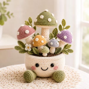 Può includere: Una composizione all'uncinetto con un vaso centrale color crema dal volto sorridente, due piedi verdi e vari funghi colorati nelle tonalità del verde, rosa, giallo, viola e azzurro, arricchita da piccoli fiori bianchi e foglie verdi.