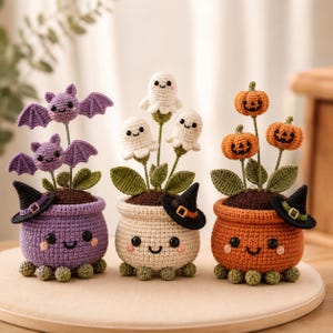 May include: Three crocheted potted plants featuring smiling faces. The left pot is purple with two bats, the centre pot is cream with three ghosts, and the right pot is orange with three jack-o'-lanterns. Each pot wears a small witch hat.