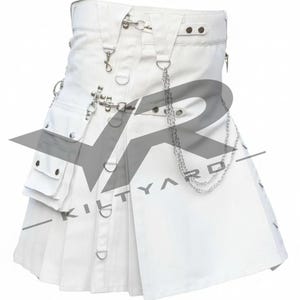 May include: A white utility kilt featuring a pleated design, multiple cargo pockets with silver-toned snap buttons, metal D-rings, and decorative silver chains attached to the waistband. The garment includes adjustable straps and metal hardware.