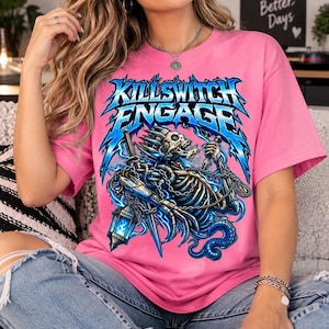 May include: A bright pink short-sleeve t-shirt featuring a graphic print of a skeletal figure in blue armour holding a lantern and a sword. The text Killswitch Engage is printed in a stylised blue font above the skeletal figure on the front.