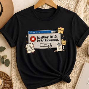 May include: A black short-sleeved t-shirt featuring a graphic of a computer system error window with the text Adulting: 0/10. Do Not Recommend. The design includes a To-Do list, a coffee mug labeled It's Fine, and sticky notes with text.
