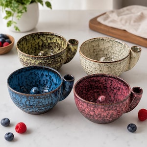 Könnte beinhalten: Vier Rasierschalen aus Keramik in Gelb, Creme, Blau und Pink, jede mit einer texturierten, gesprenkelten Glasur, einem kleinen seitlichen Griff und einer erhöhten Erhebung am Boden des Innenbeckens zum Aufschäumen von Rasierseife.